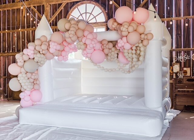 white bouncy castle with pink balloon decor for weddings or children's parties.