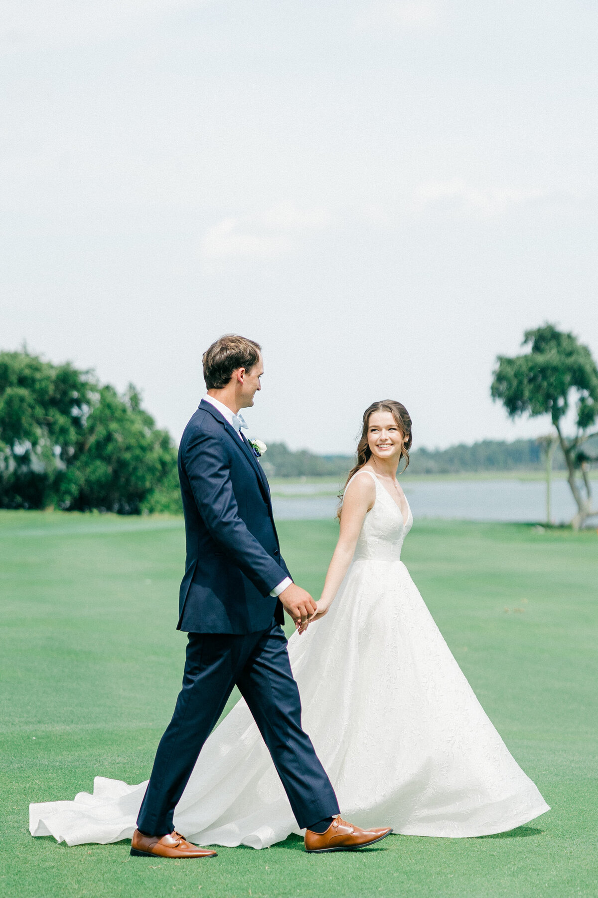 Groom leads his smiling bride across the waterfront fairway at Dataw Island Club, South Carolina—captured by luxury wedding photographer Amia Marcell.