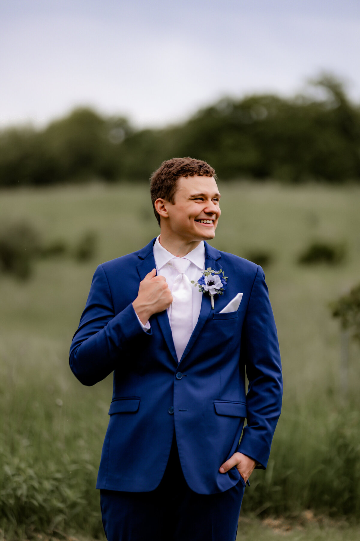 A groom holds his jacket and laughs into the distance.
