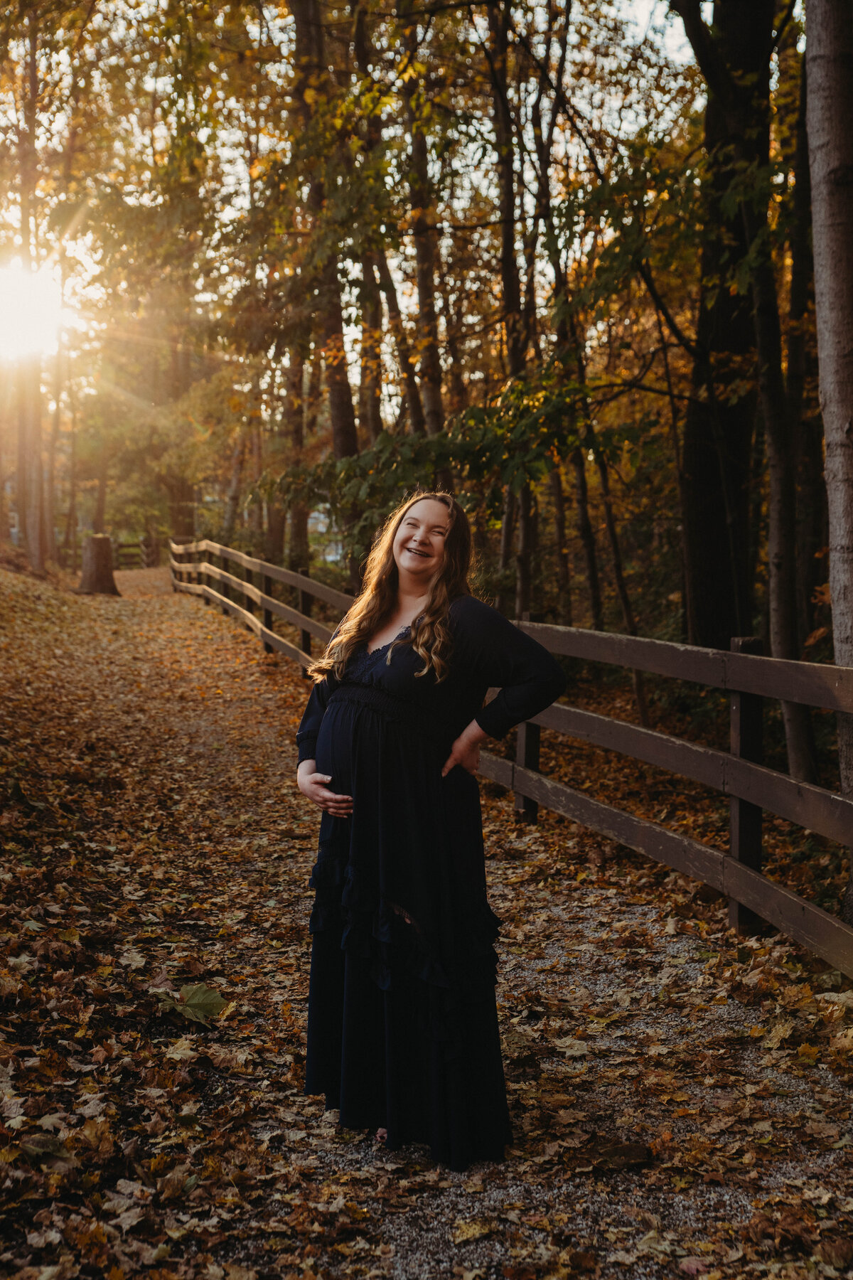 Pregnant woman stands in setting sun during fall at Olmsted Falls park.