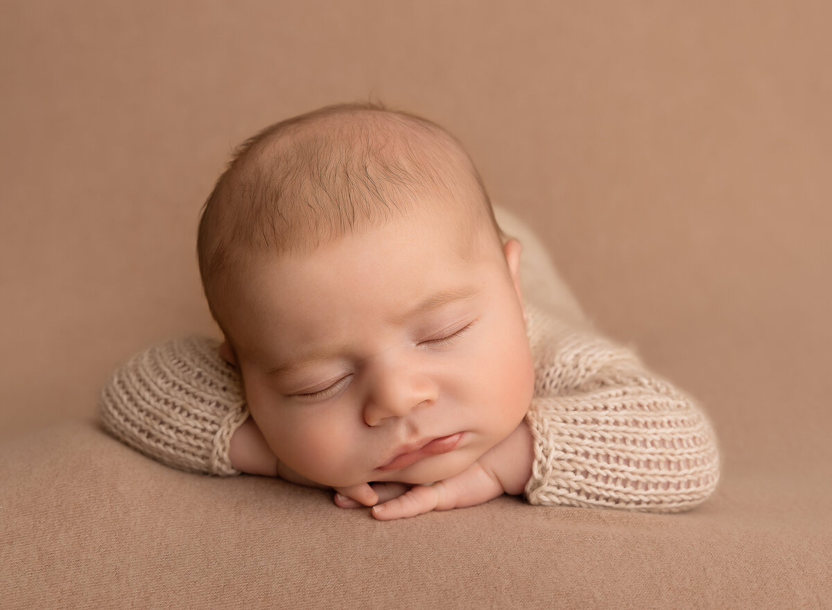 Baby boy is sleeping on his belly with his hands folded under his chin. Captured by top Brooklyn newborn photographer Chaya Bornstein