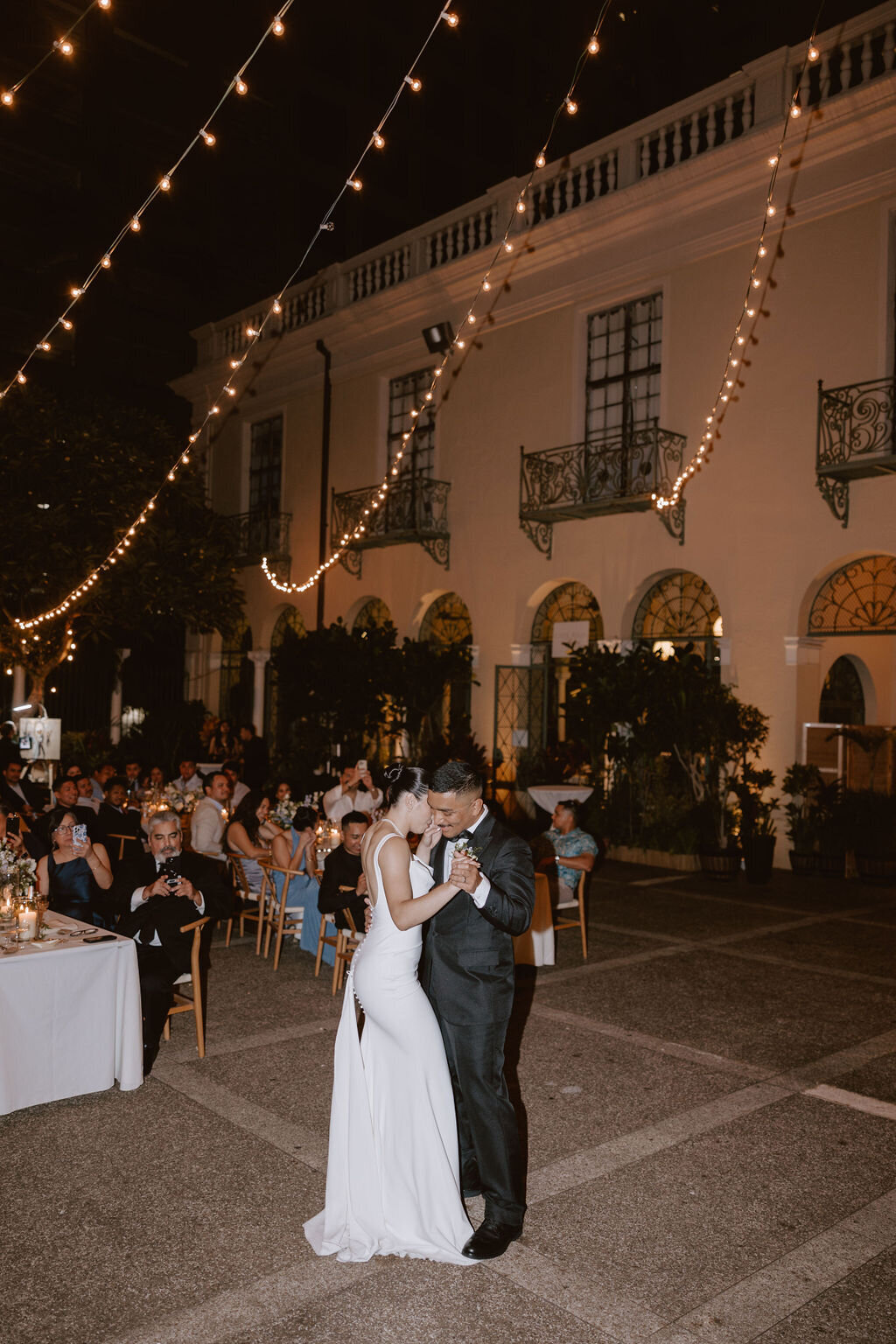 Bride and groom first dance in front of all their guests at cafe julia under twinkle lights