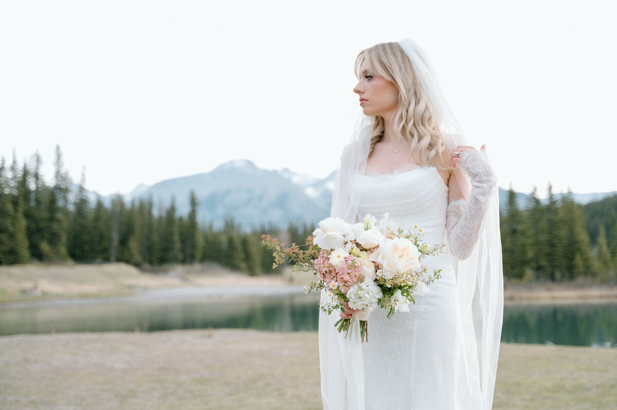 Bride holding floral bouquet with dramatic mountains behind her at Banff wedding.