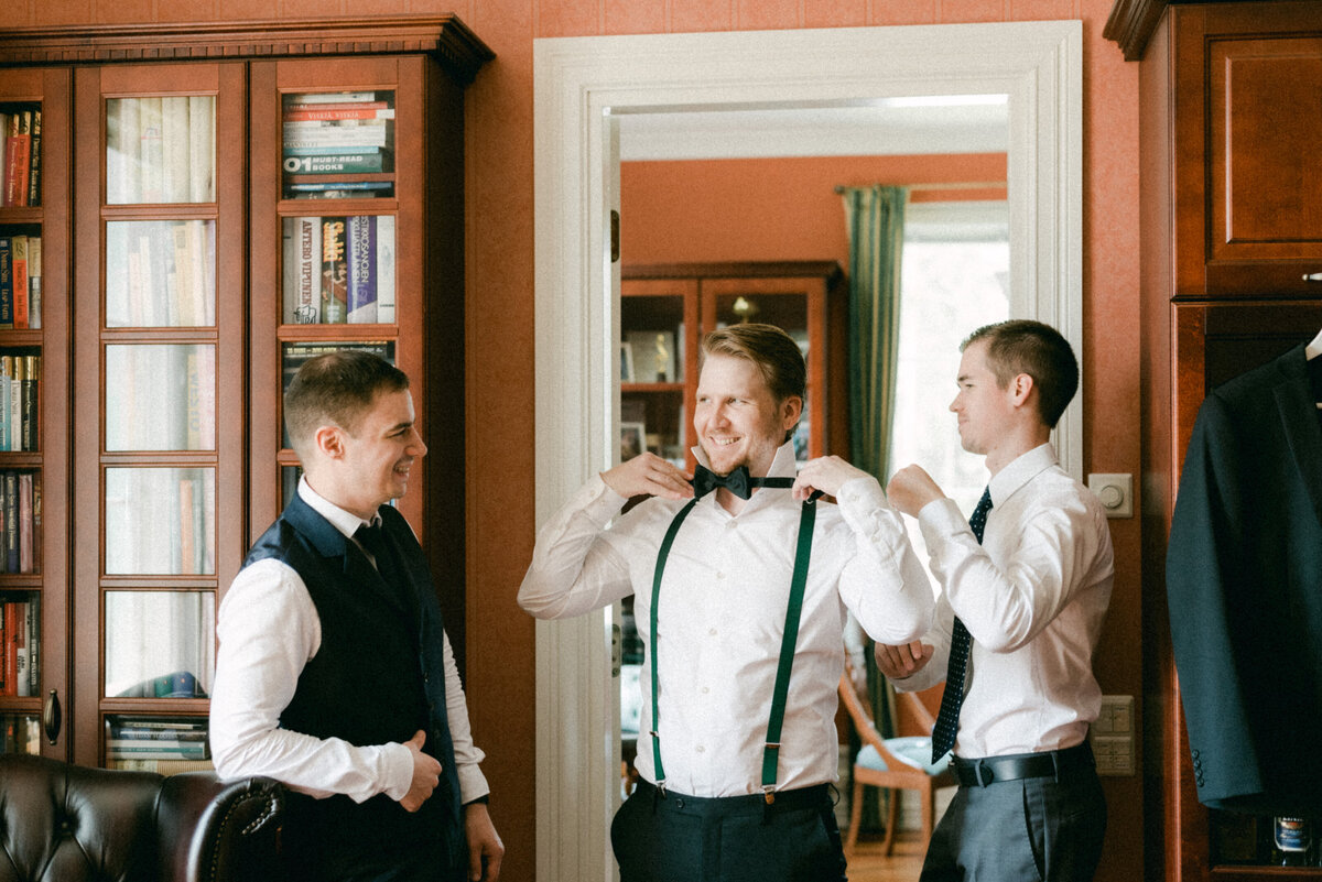 The bestman is helping the groom to put on the bowtie in an image captured by wedding photographer Hannika Gabrielsson.