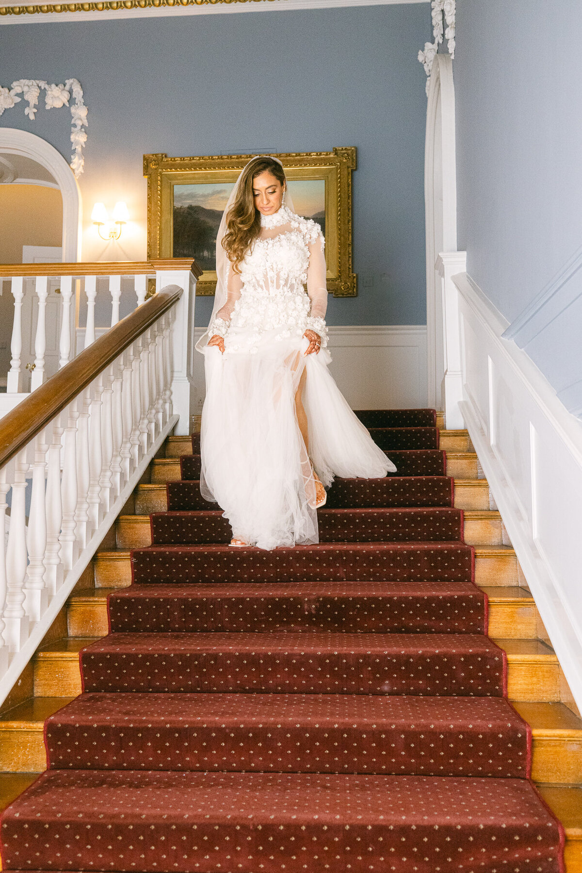 A wedding photo of the bride walking down a staircase in her white wedding dress