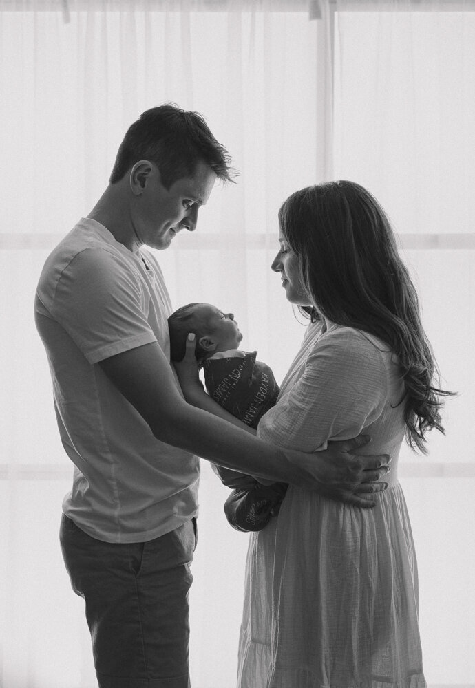 Mom and Dad hold their newborn between them and admire their baby