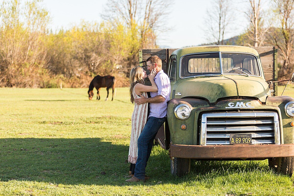 Country couple kissing on ranch near truck and horses