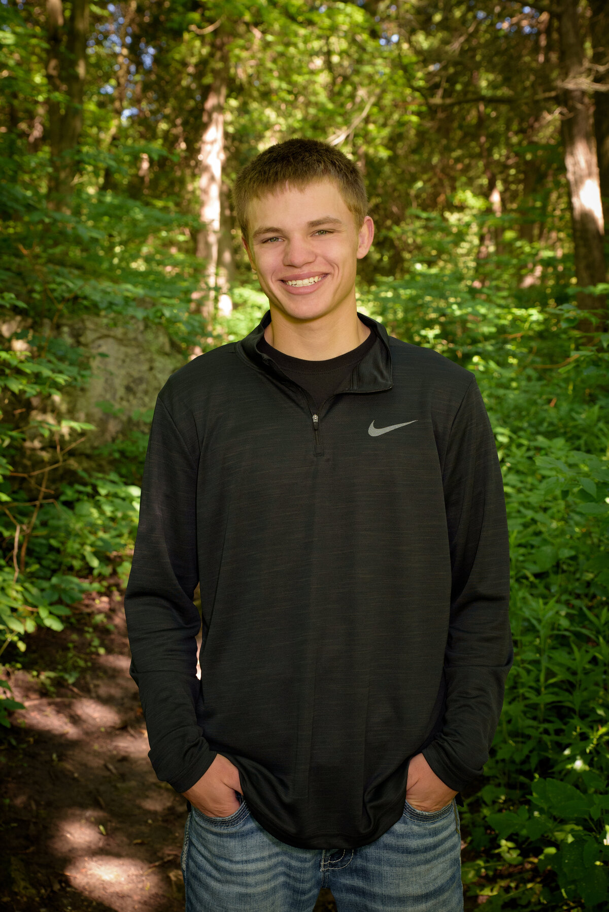 Luxemburg Casco high school senior boy wearing a long sleeve black shirt and jeans standing in the woods along a walking path at Devil's River Campground near Green Bay, Wisconsin.