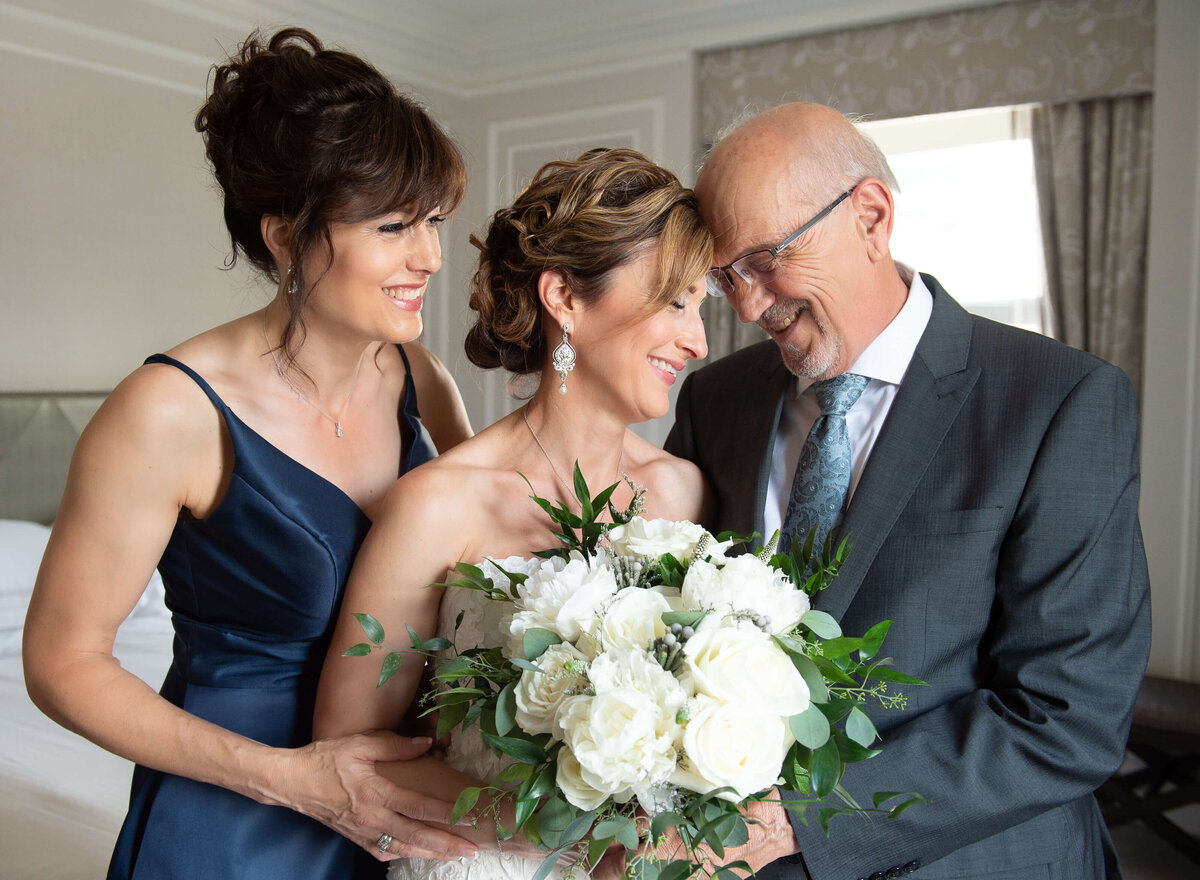 bride receiving a warm hug from her father and sister as she get ready for her Ottawa wedding