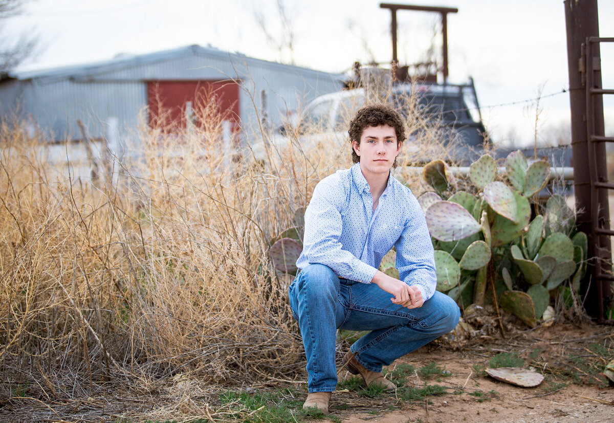 senior boy crouching down in front of cactus