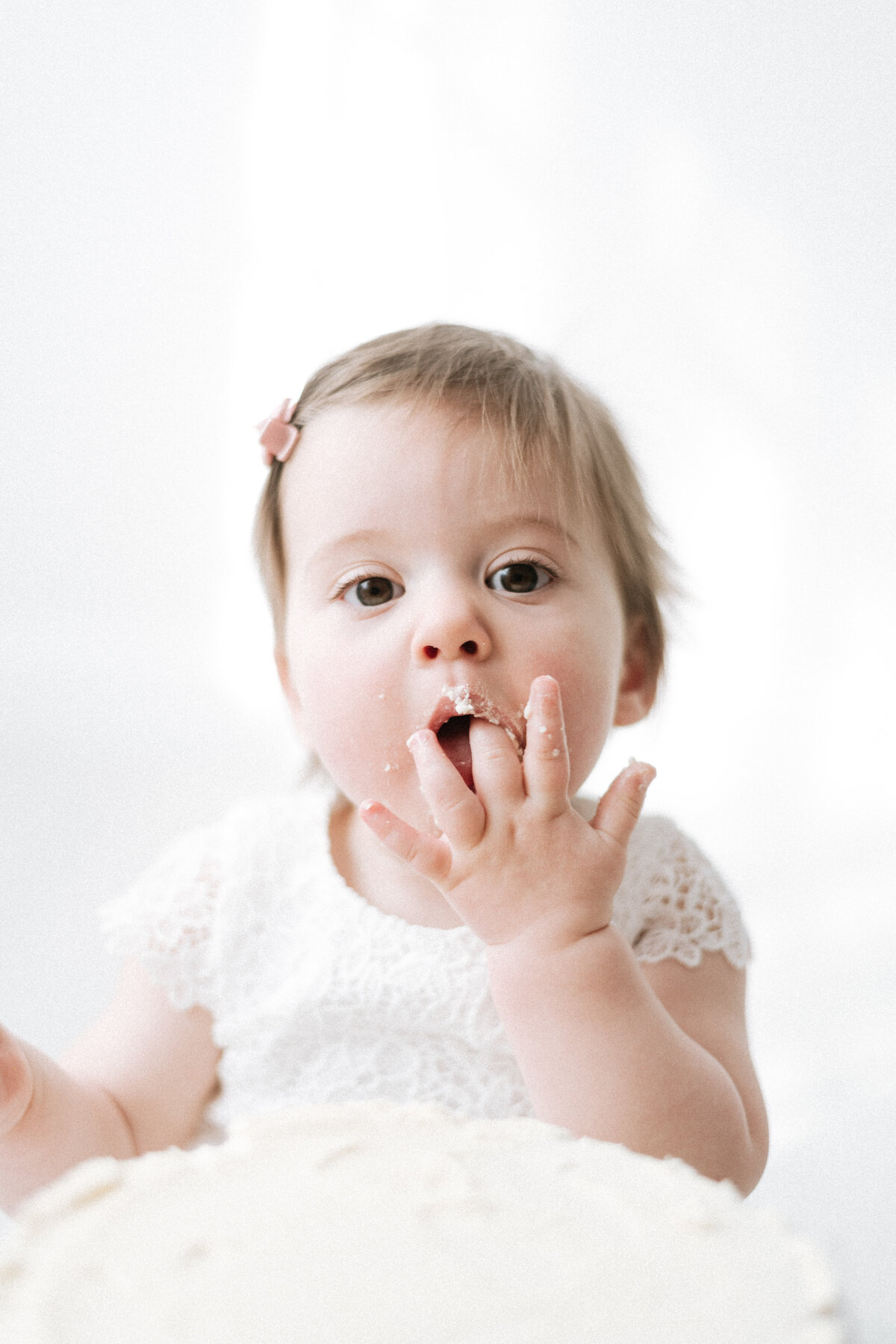 baby girl eating cake off her hand at west sussex cake smash photoshoot