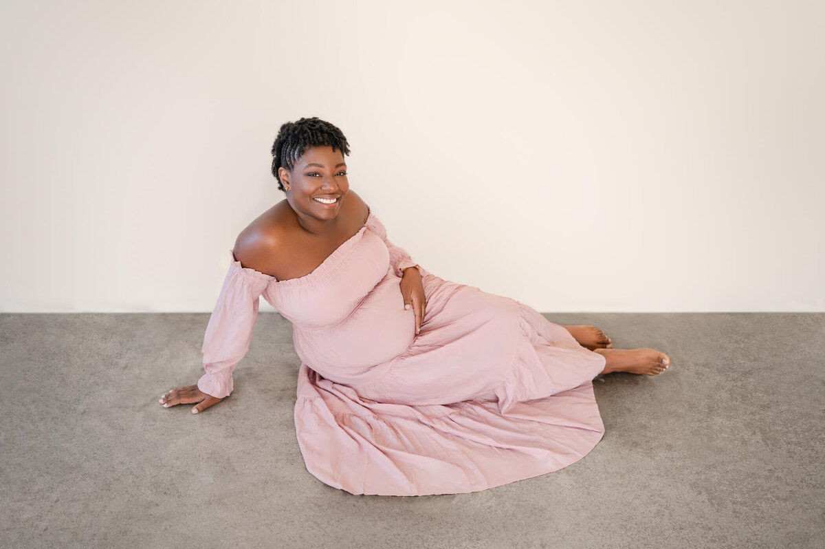 pregnant woman smiling at the camera while laying on the floor getting photos taken