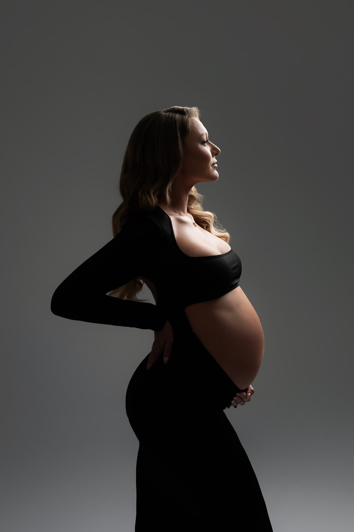 Minimalist maternity silhouette portrait highlighting baby bump curves in studio setting