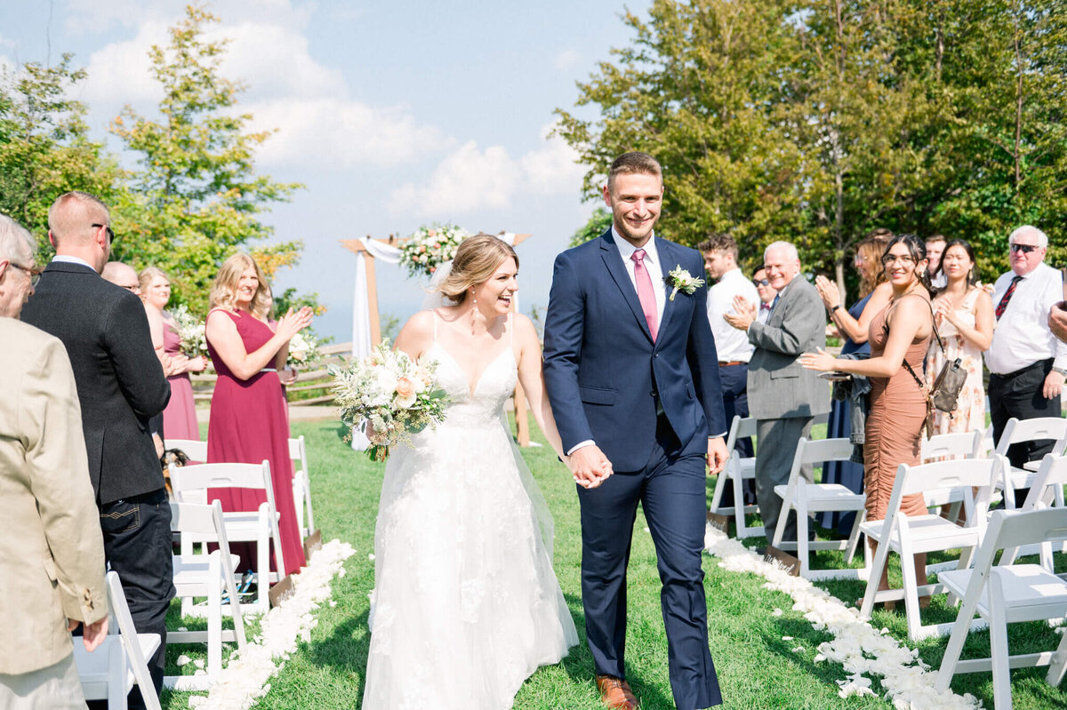 Bride and groom walking up the aisle with family and friends clapping behind them captured by Toronto wedding photographer