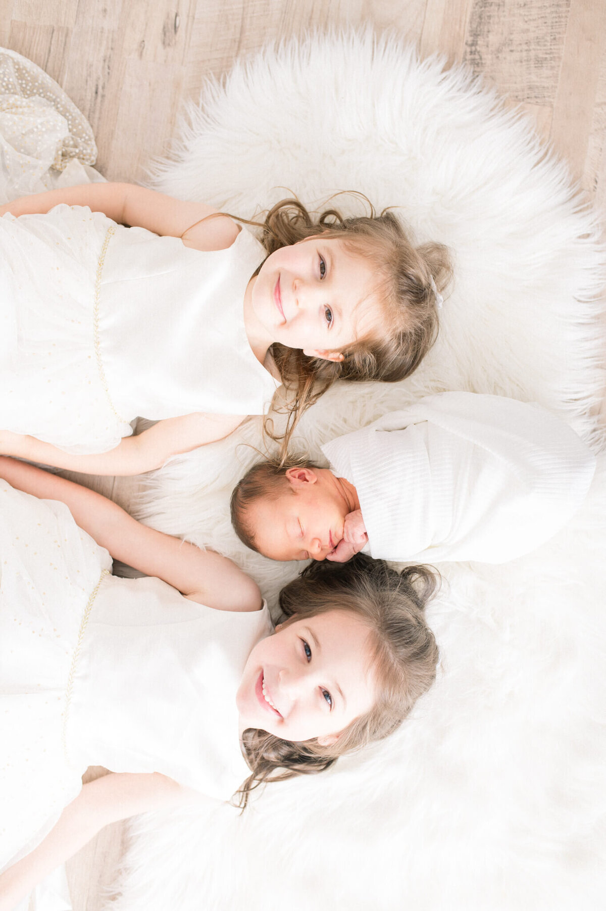 two older sister lay with newborn sister for Niagara Newborn photographer