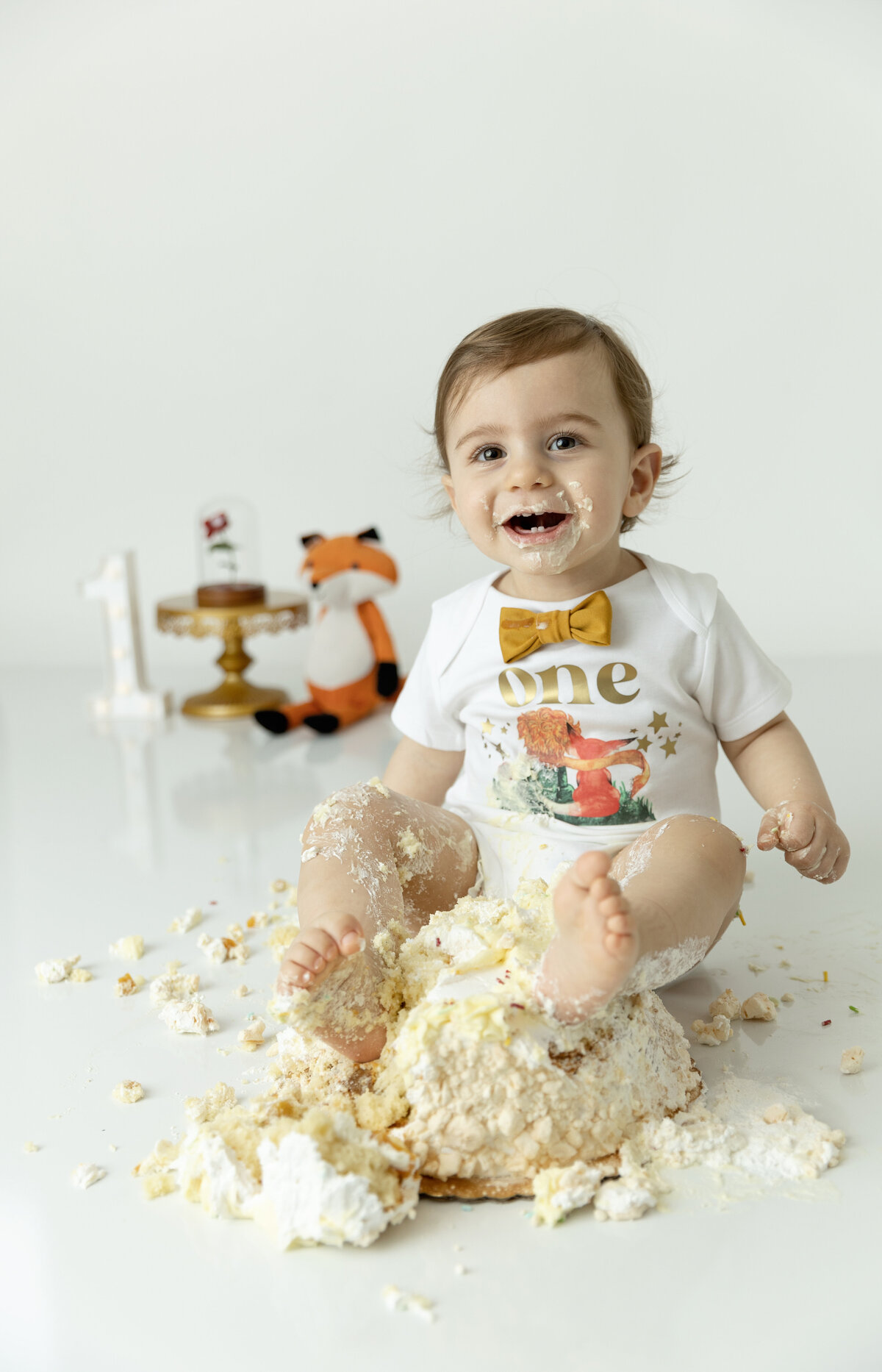 A happy young toddler boy plays and makes a mess in a studio while destroying a cake
