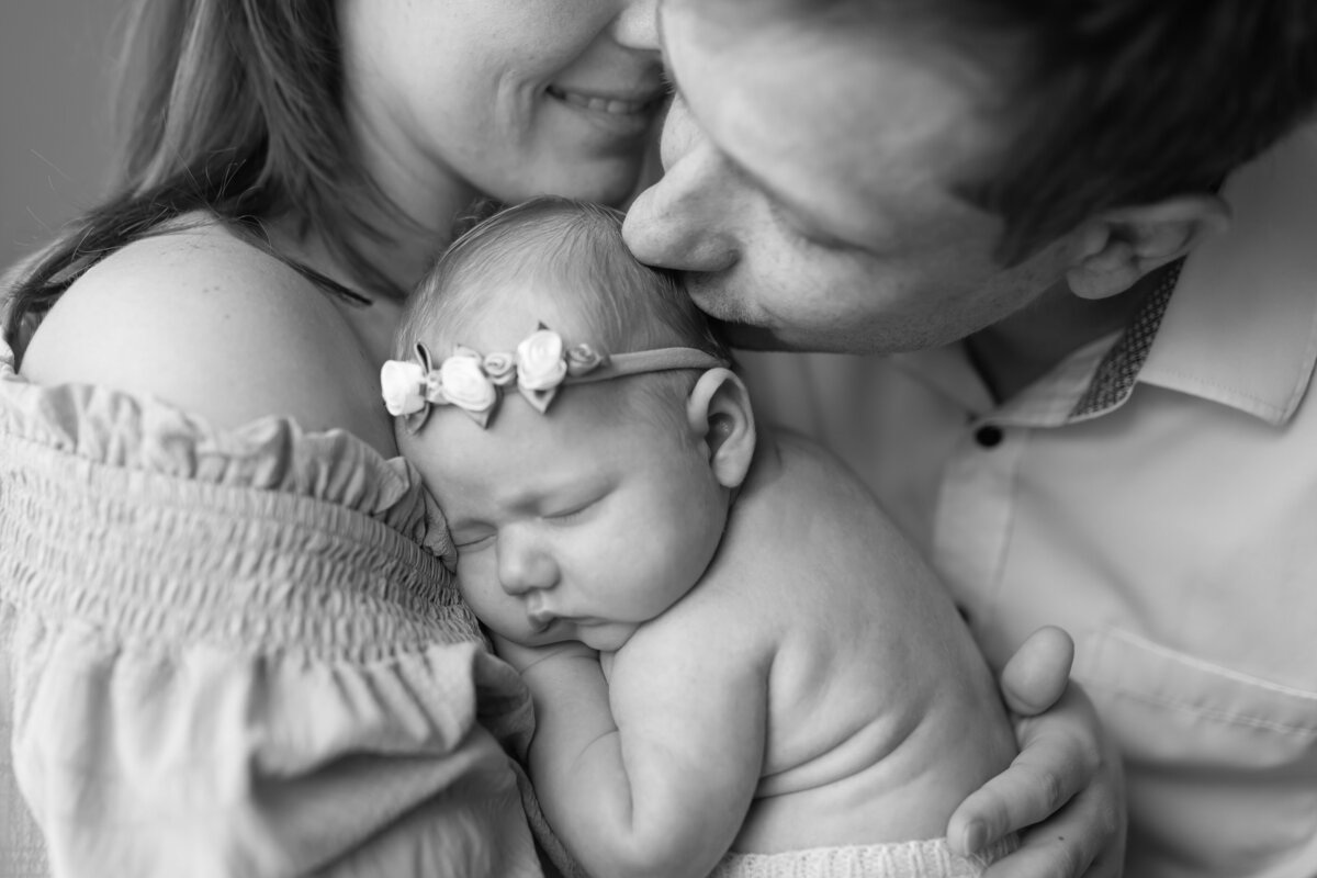 Mother holding her child while the father kisses the babies head