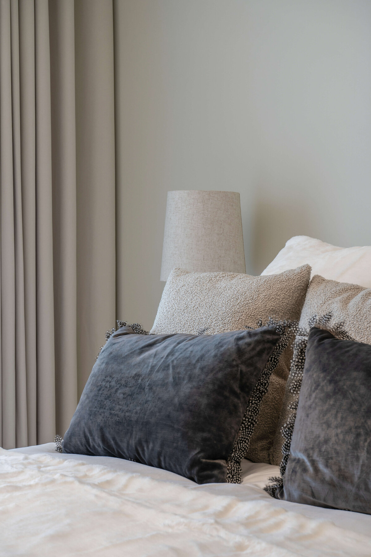 Soft neutral pillows arranged on a white bed in a cool and airy guest bedroom.