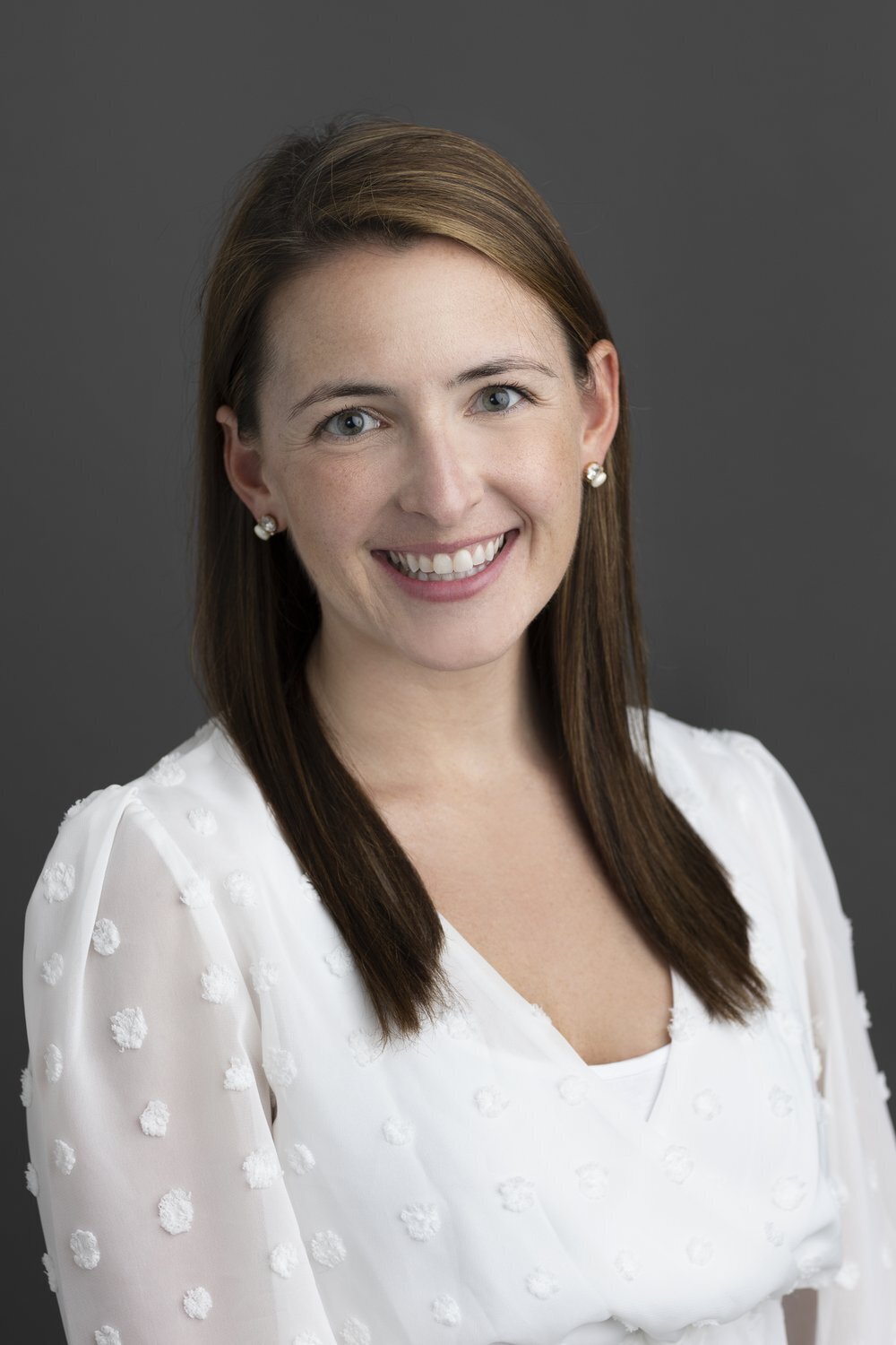 Smiling woman in white blouse on gray backdrop