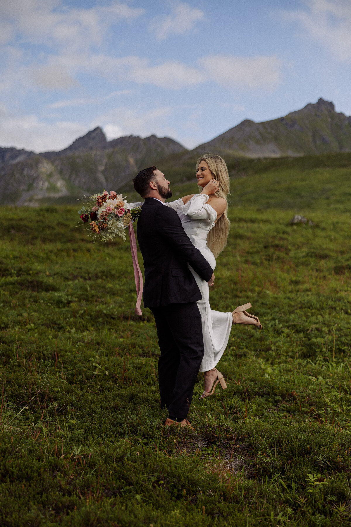 A person lifting up their partner as they both smile in a field 