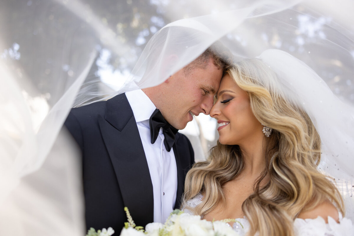 A bride and groom forehead to forehead under a veil