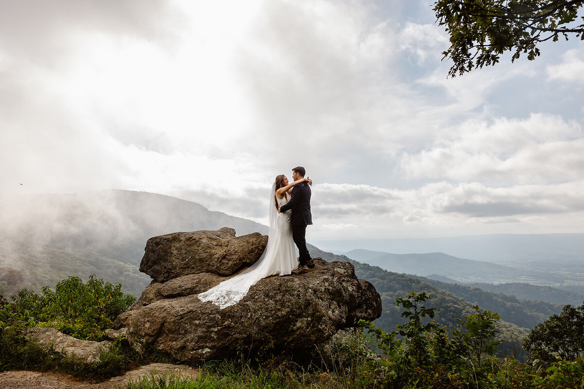 Newlyweds hugging and standing on a large rock