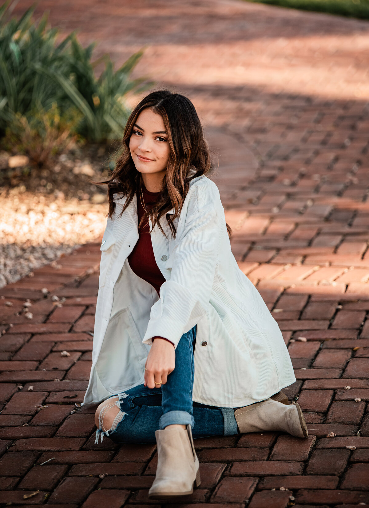 A local senior sits on a red brick walkway with a white jacket on.