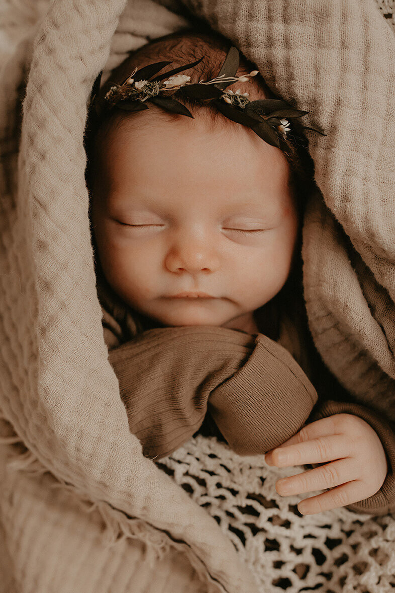a baby girl wrapped in textiles while wearing a leaf headband