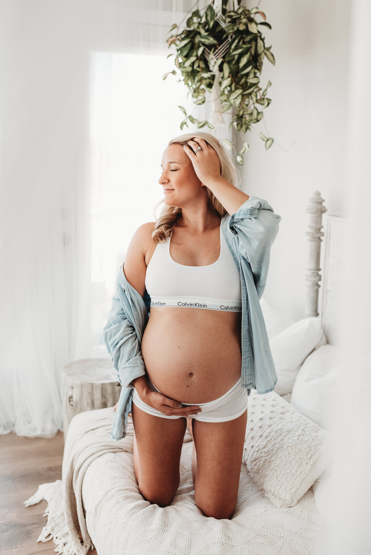 pregnant woman holding bare belly wearing blue button down shirt and calvin klein underwear