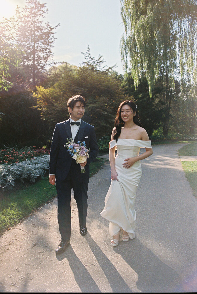 Groom holds a bouquet while walking with his bride toward the wedding hall at Botanical Garden