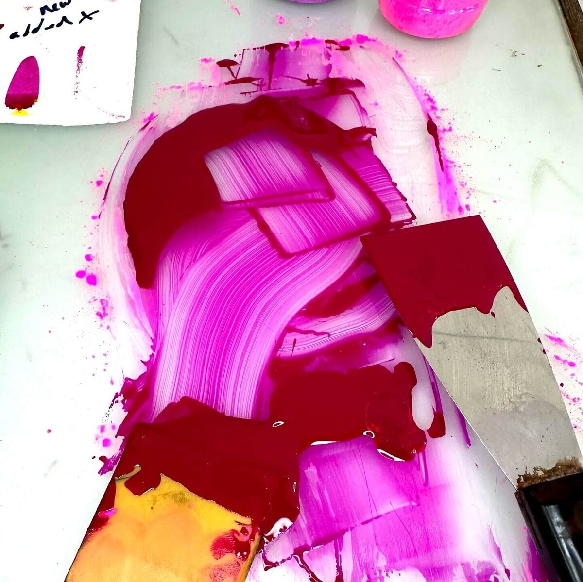 A swirled blend of deep magenta and pink ink on a glass surface with palette knives—expressive color in motion.