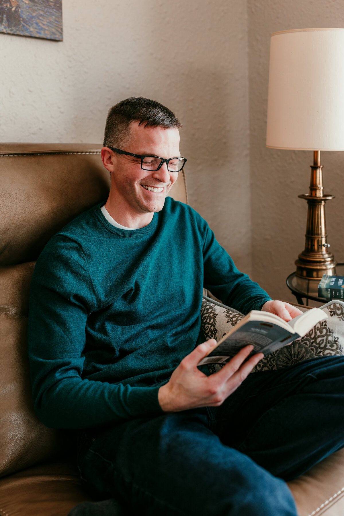 Man sitting comfortably on a couch with a book in hand, showcasing personality and charm for online dating profiles.