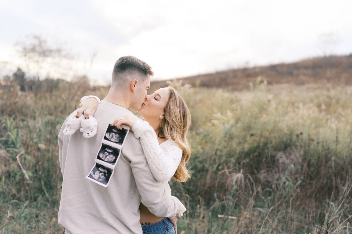 husband kisses pregnant wife in field during golden hour in knoxville tennessee