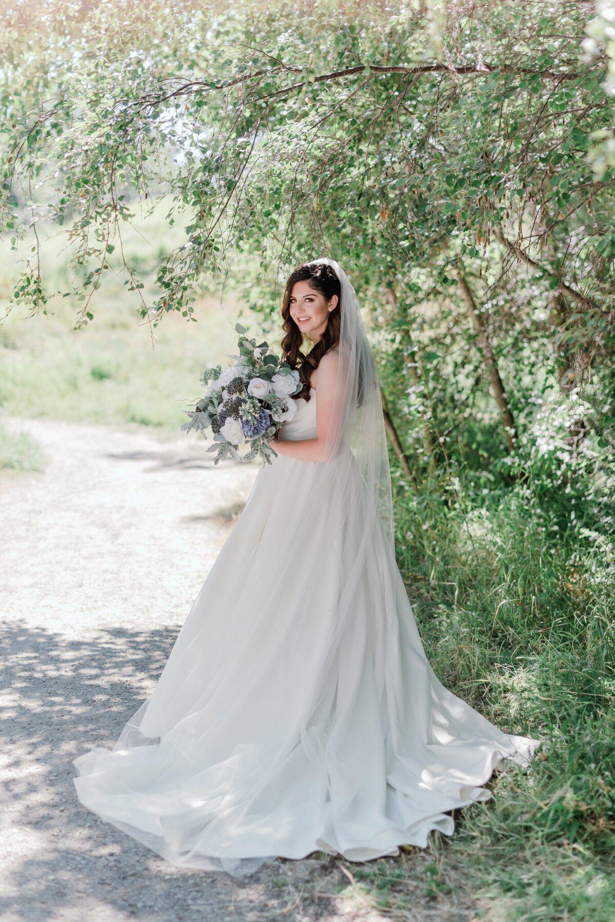 Gorgeous and elegant bride in beautiful satin gown, veil, and bouquet with blue, purple and white flowers, captured by Kaity Body Photography, elegant film inspired wedding photographer in Calgary, Alberta. Featured on the Bronte Bride Vendor Guide.