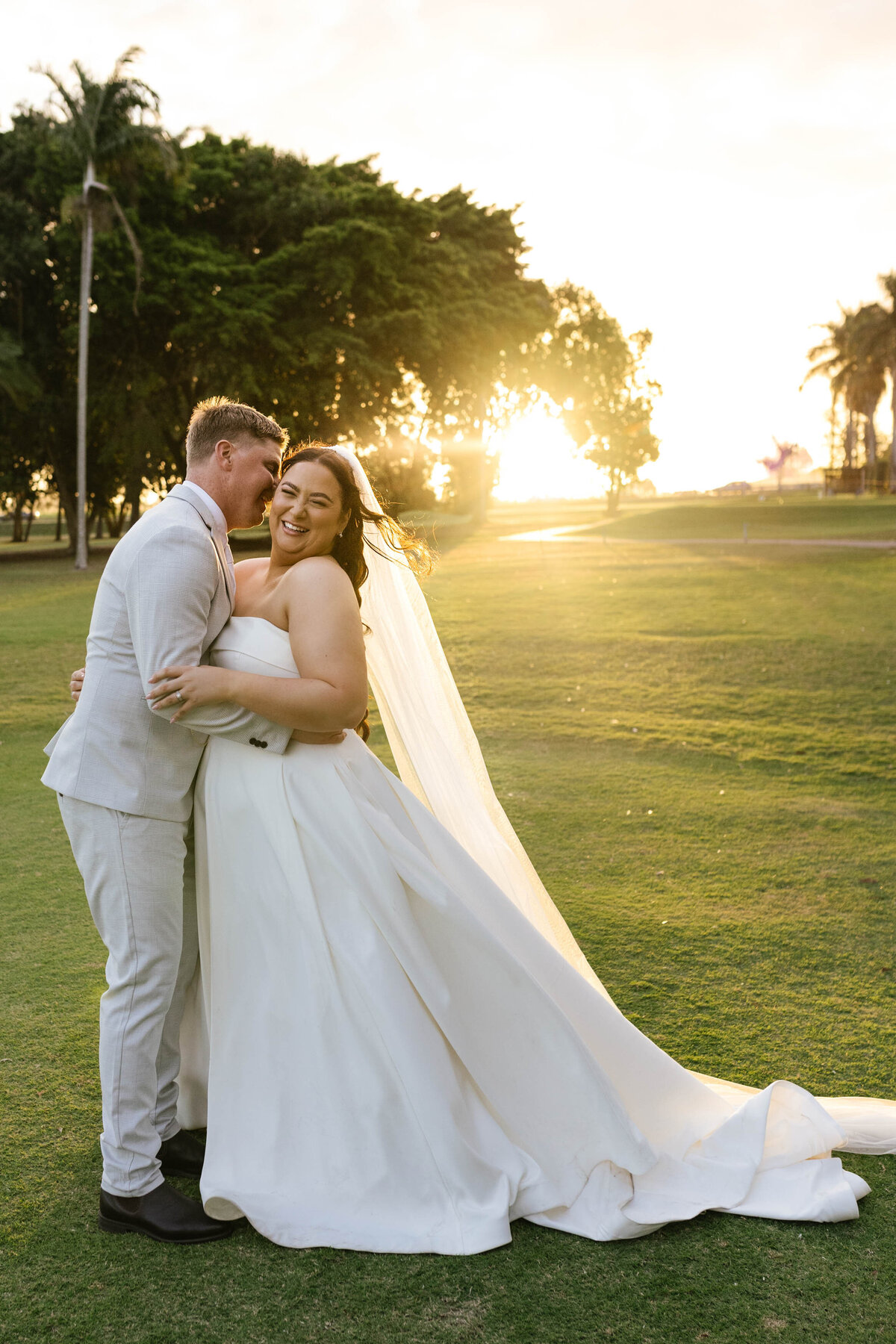 Bride giggles cutly as her partner whispers into her ear with the sun setting in the background. 