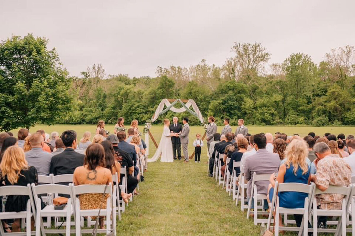 Wedding ceremony with guests seated outdoors, officiant in center