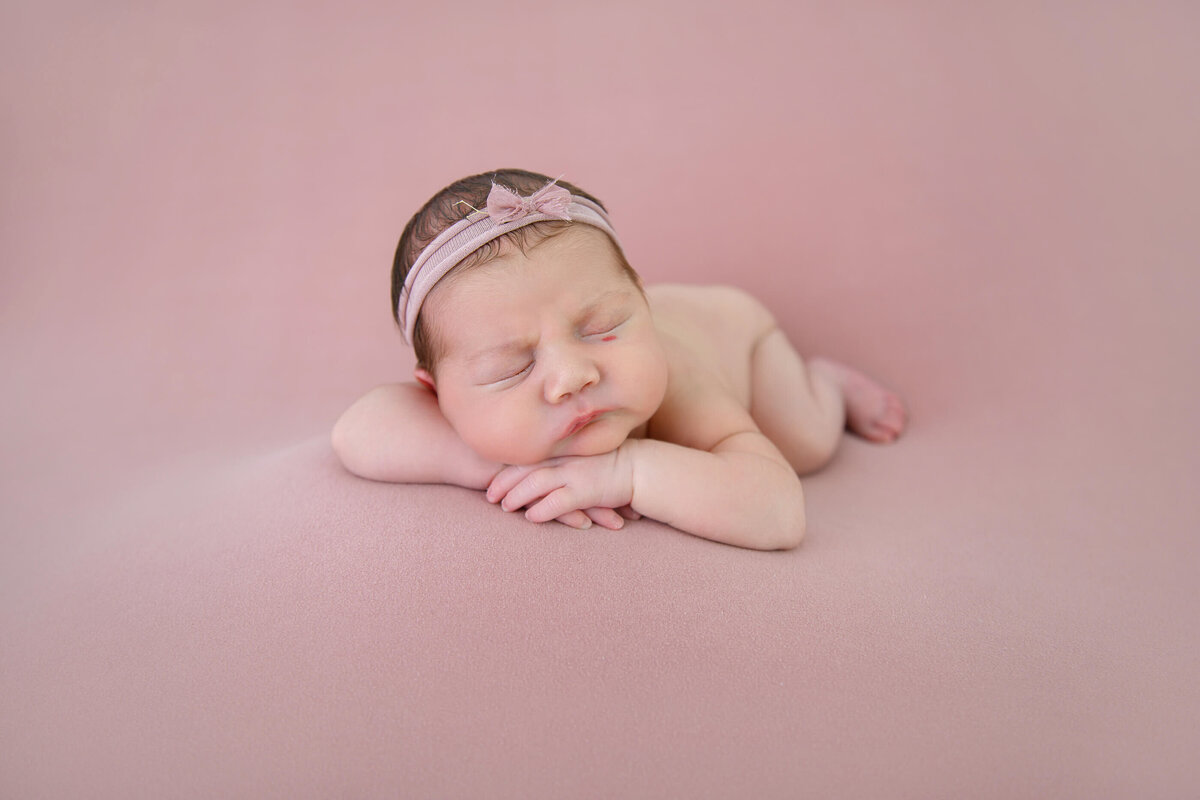 newborn girl laying on a pink background for a monochromatic image for her newborn photography session 