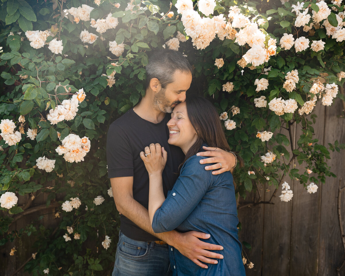 Couple embrace under rose bush in front of their house