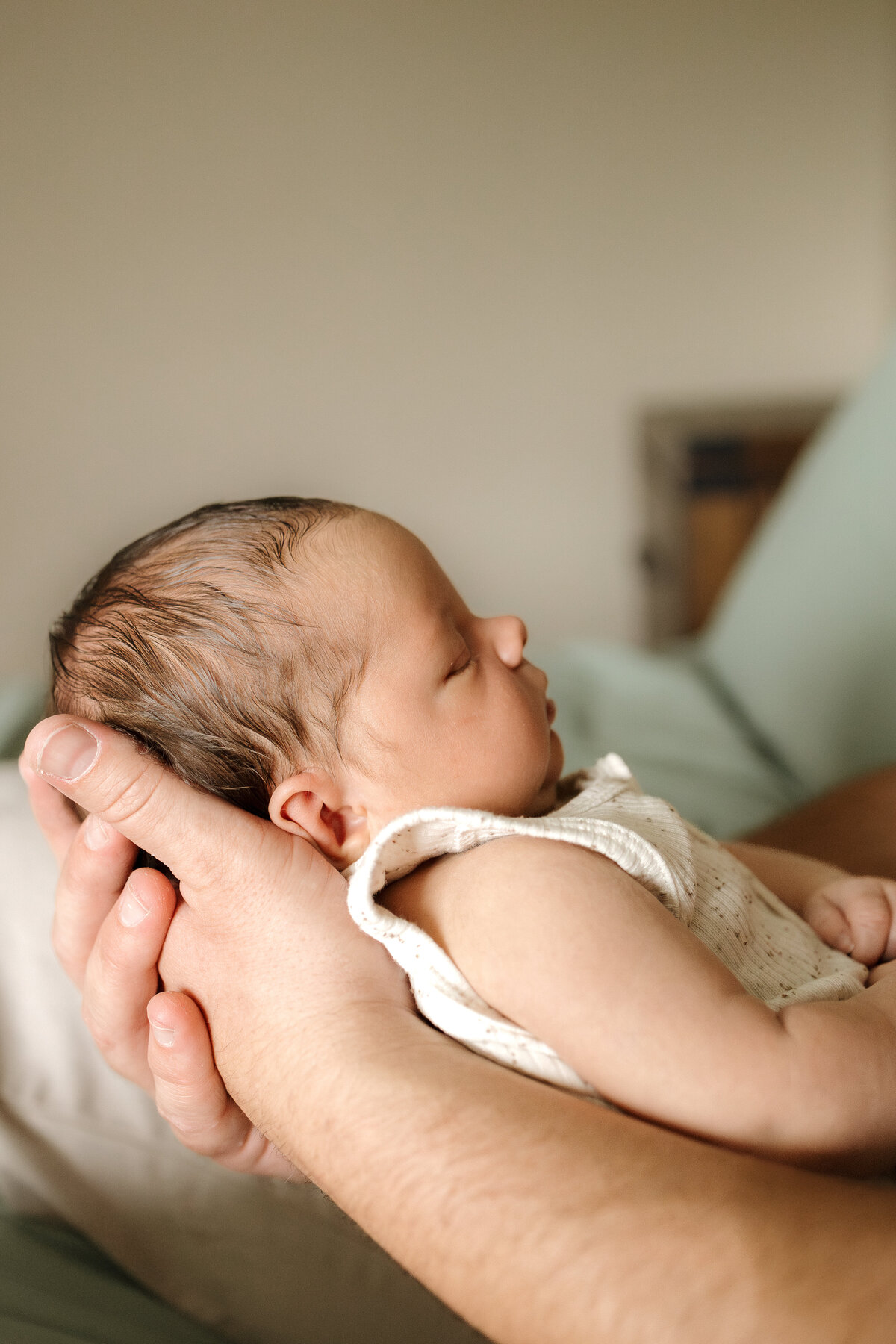 dad holding newborn baby boy with camera capturing baby's profile during lifestyle in home newborn session with alexis adkins photo in longmont colorado