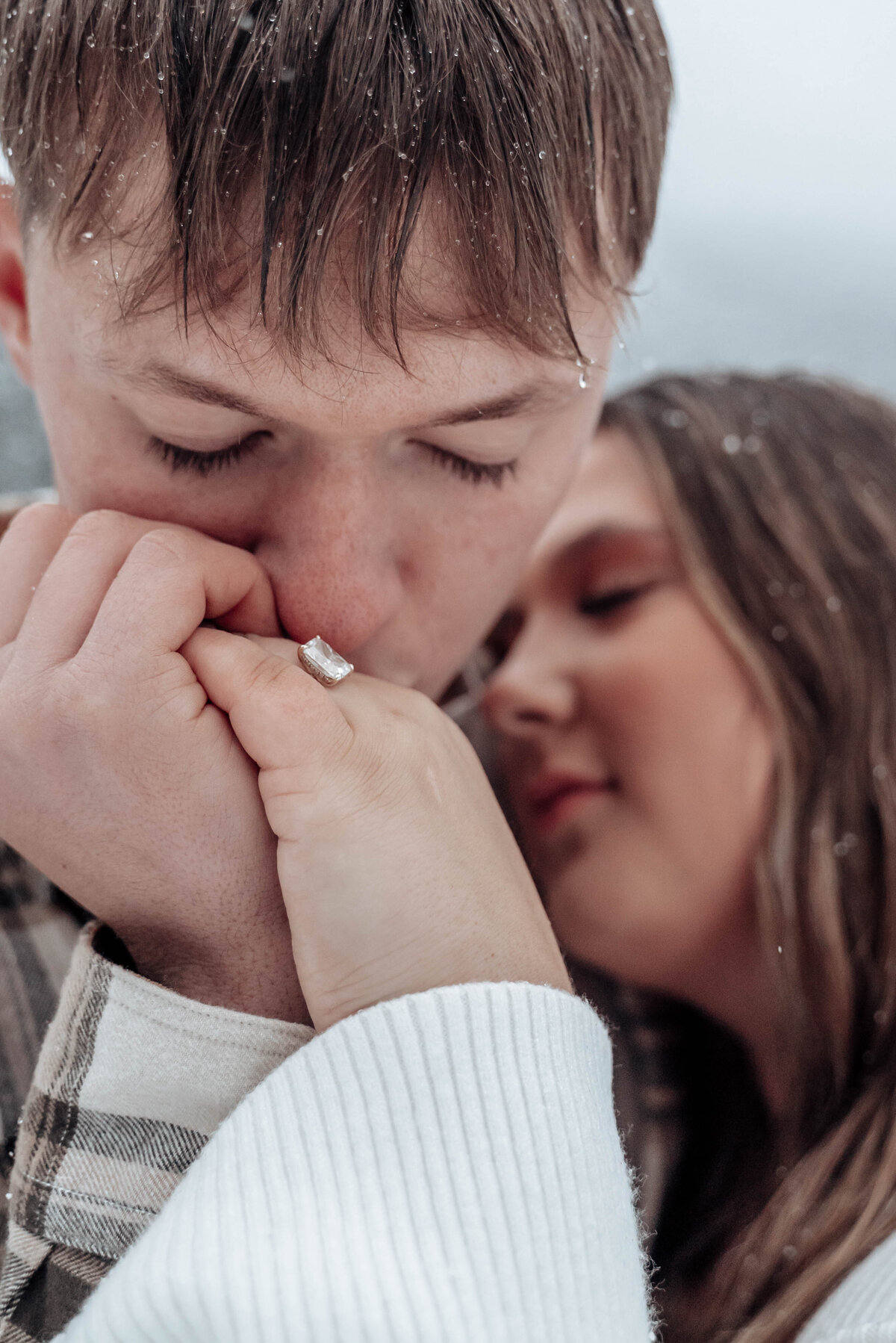 Close-up of groom-to-be kissing fiancée’s hand in soft snowstorm.