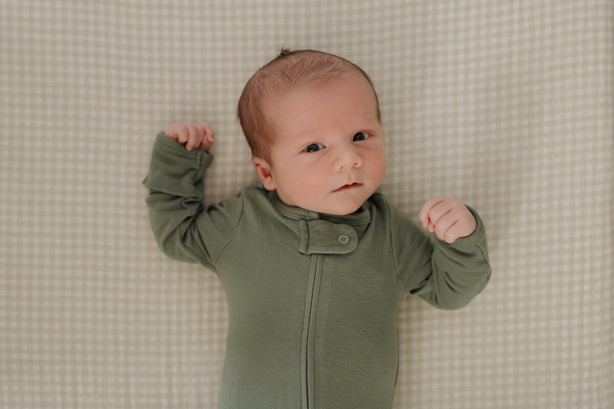 Newborn laying in crib on gingham sheet in green onesie during in home newborn session in longmont colorado