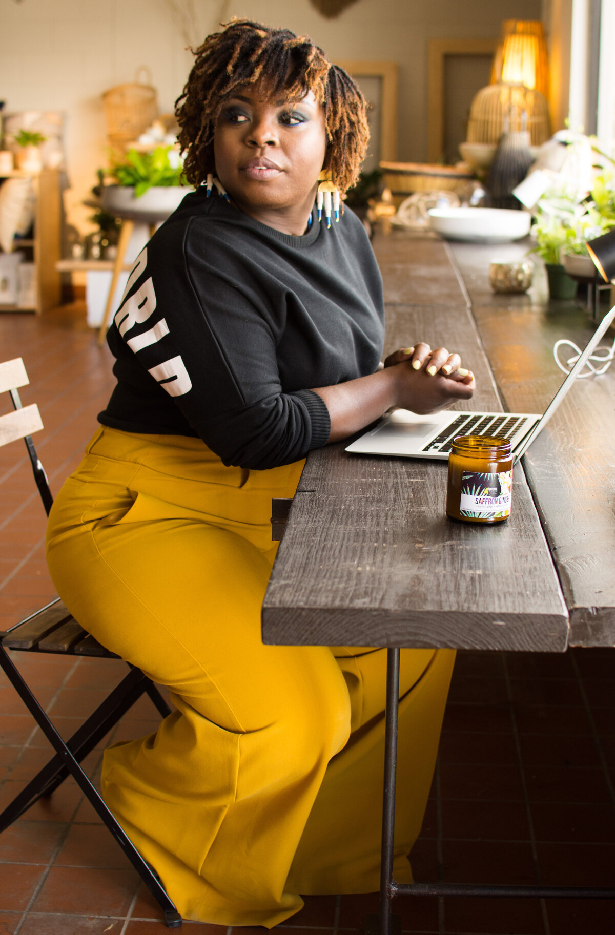Annie Brown of NaturalAnnie Essentials sits at a long wooden table with a laptop and one of her business' candles