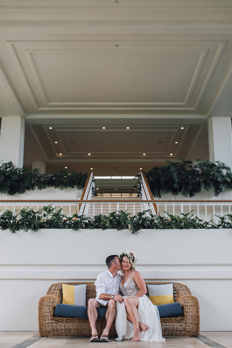 Groom kissing bride on  a navy couch with yellow pillows at the Four Seasons Oahu