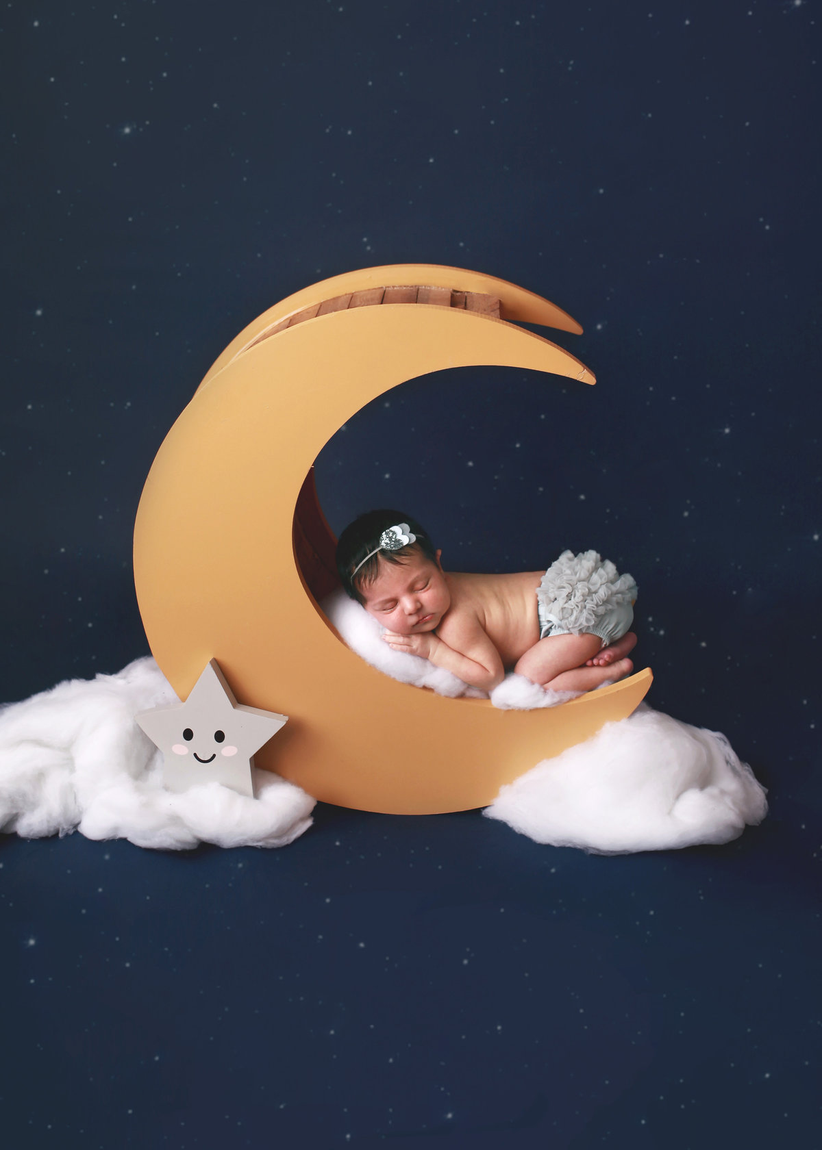 newborn baby posed on moon prop with clouds against starry backdrop