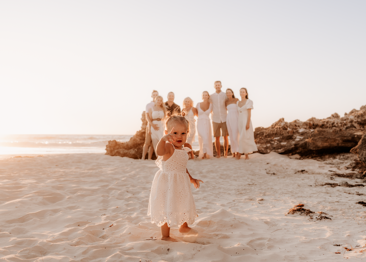 An extended family in the background looking at their cute toddler at Mullaloo Beach  in Perth WA