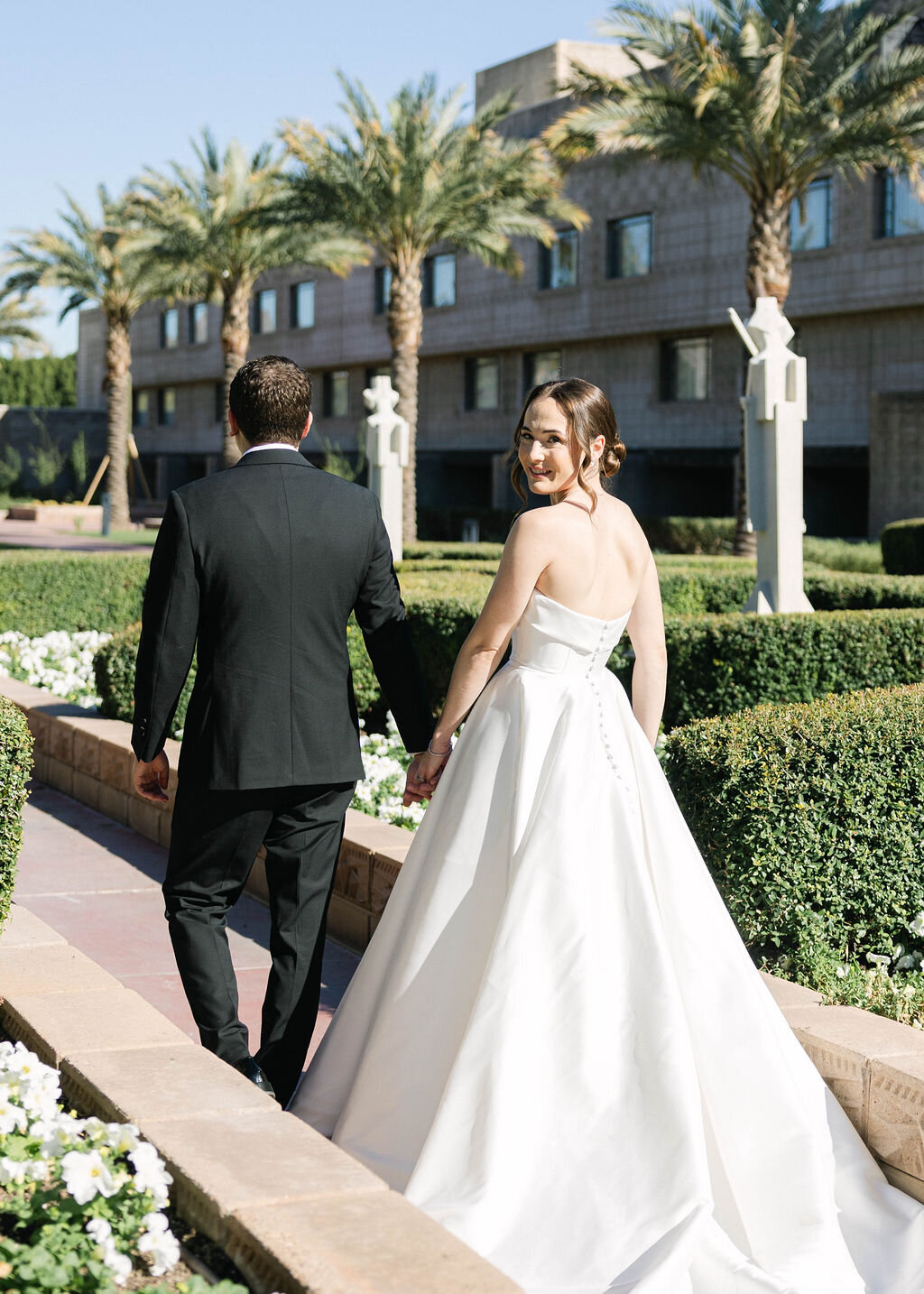 Bride and groom walking hand in hand through the Arizona Biltmore garden pathway.
