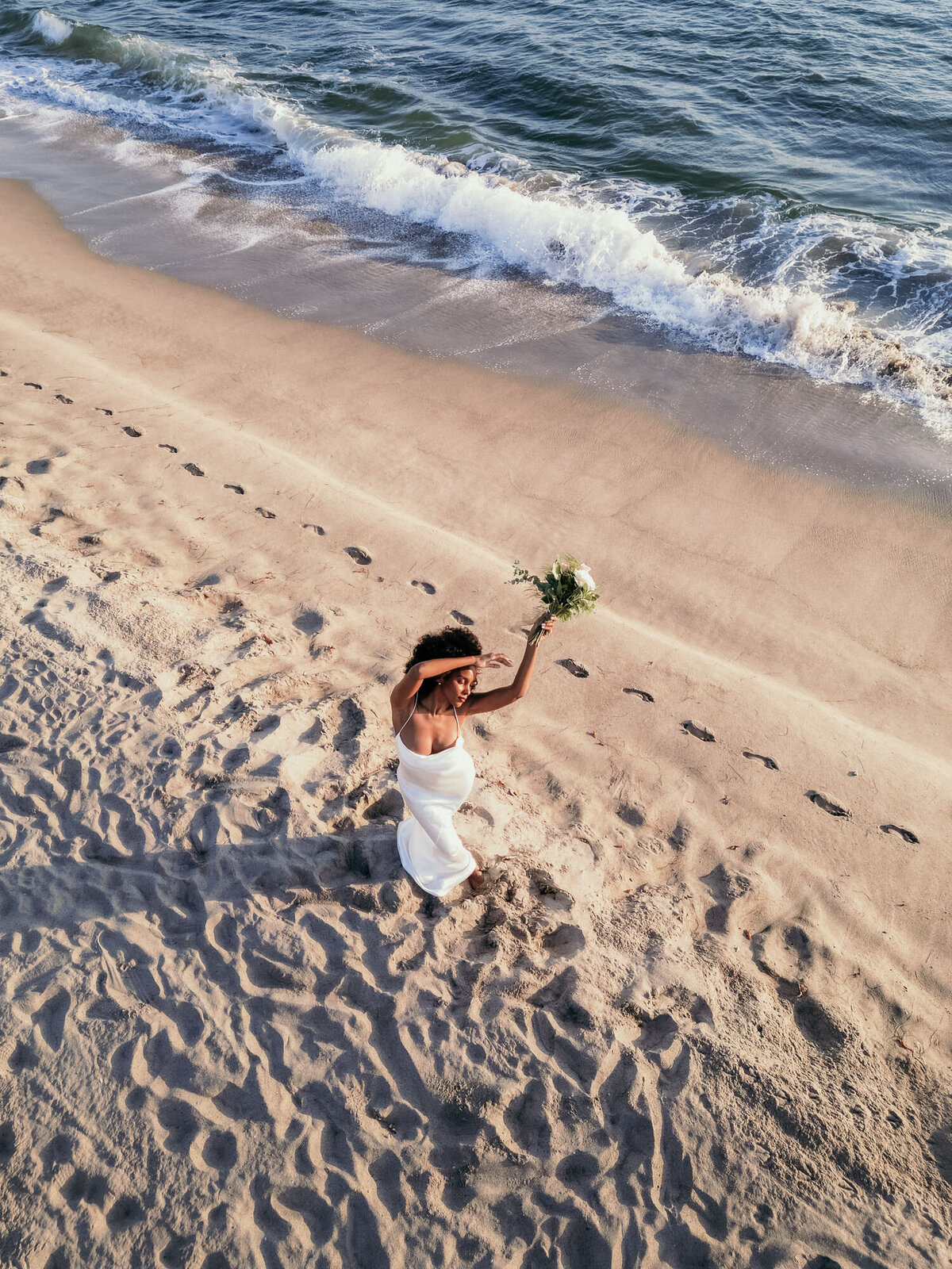 Dieses Drohnenfoto zeigt wie die Braut mit ihrem Strauß am Meer tanzt.