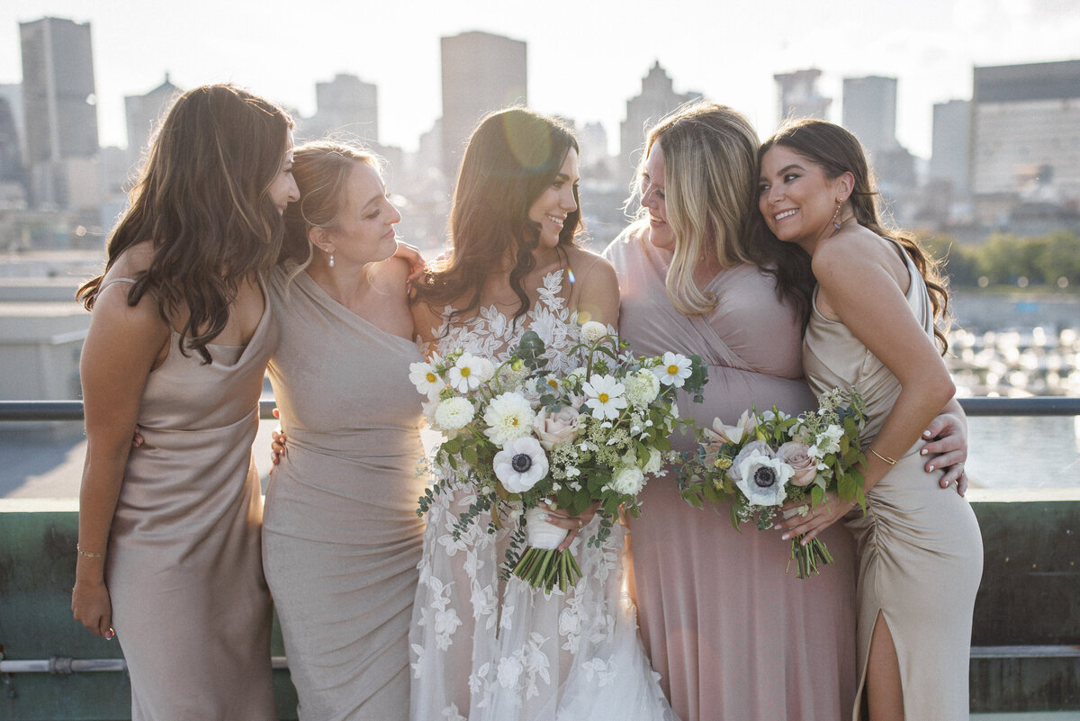A bride and her bridesmaids stand on the roof of the Science Centre at sunset, holding lush bouquets.