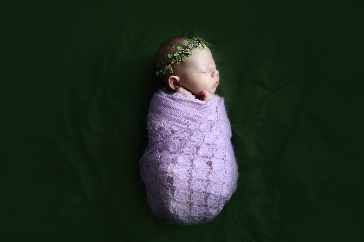 A portrait of baby girl sleeping tightly wrapped in he knitted blanket during home newborn photo session by Yuliia Terziian Photography in Calgary,Alberta.