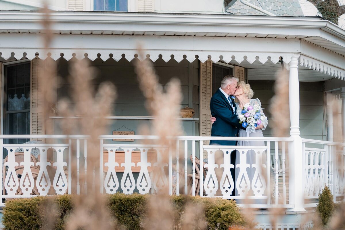 Elderly couple embrace on a porch with. Victorian railings in the distance